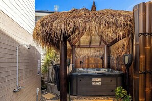 Ein Wellnessbereich und Grillplatz mit Whirlpool, Bambuswänden und einem Reetdach.