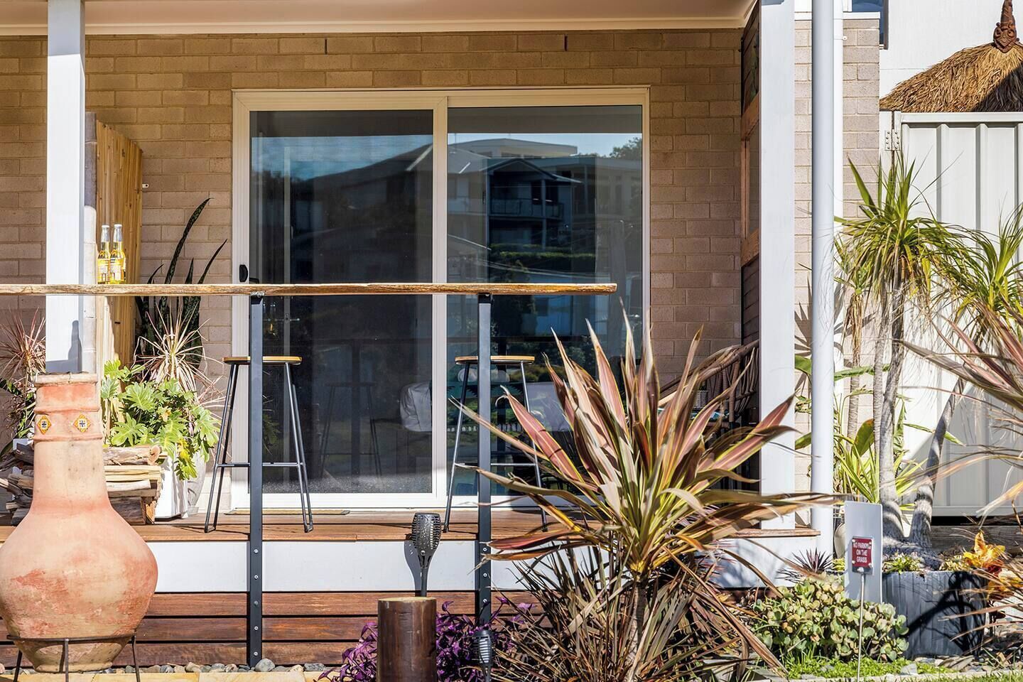 A house with a large glass door, a brick exterior, and a variety of plants in the front yard.