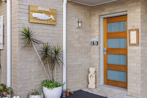 Ein Gebäude mit einer Holztür, einem Schild mit der Aufschrift 'BEACH HOUSE' und verschiedenen Topfpflanzen.