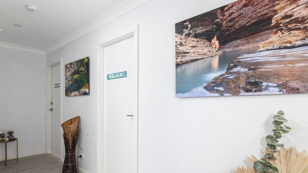 Um corredor com uma porta identificada com 'WHALE', um quadro com uma paisagem costeira e um arranjo de plantas.