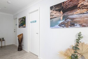 A hallway with a door labeled 'WHALE,' a framed picture of a coastal scene, and a plant arrangement. - Dolphin Studio Suite (Fishermans Bay)