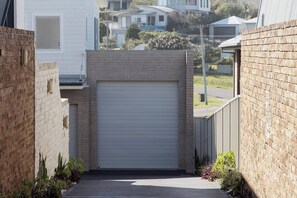 A residential garage with a closed door, surrounded by brick walls and a narrow pathway. - Dolphin Studio Suite (Fishermans Bay)