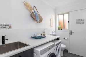 Ein modernes Badezimmer mit Waschbecken, Toilette und Waschmaschine. Ein Fenster bietet Blick ins Freie.