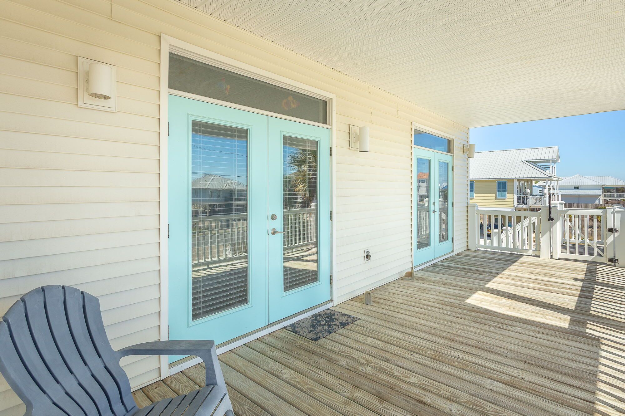 A covered porch with a wooden deck, a light blue door, and a single Adirondack chair.