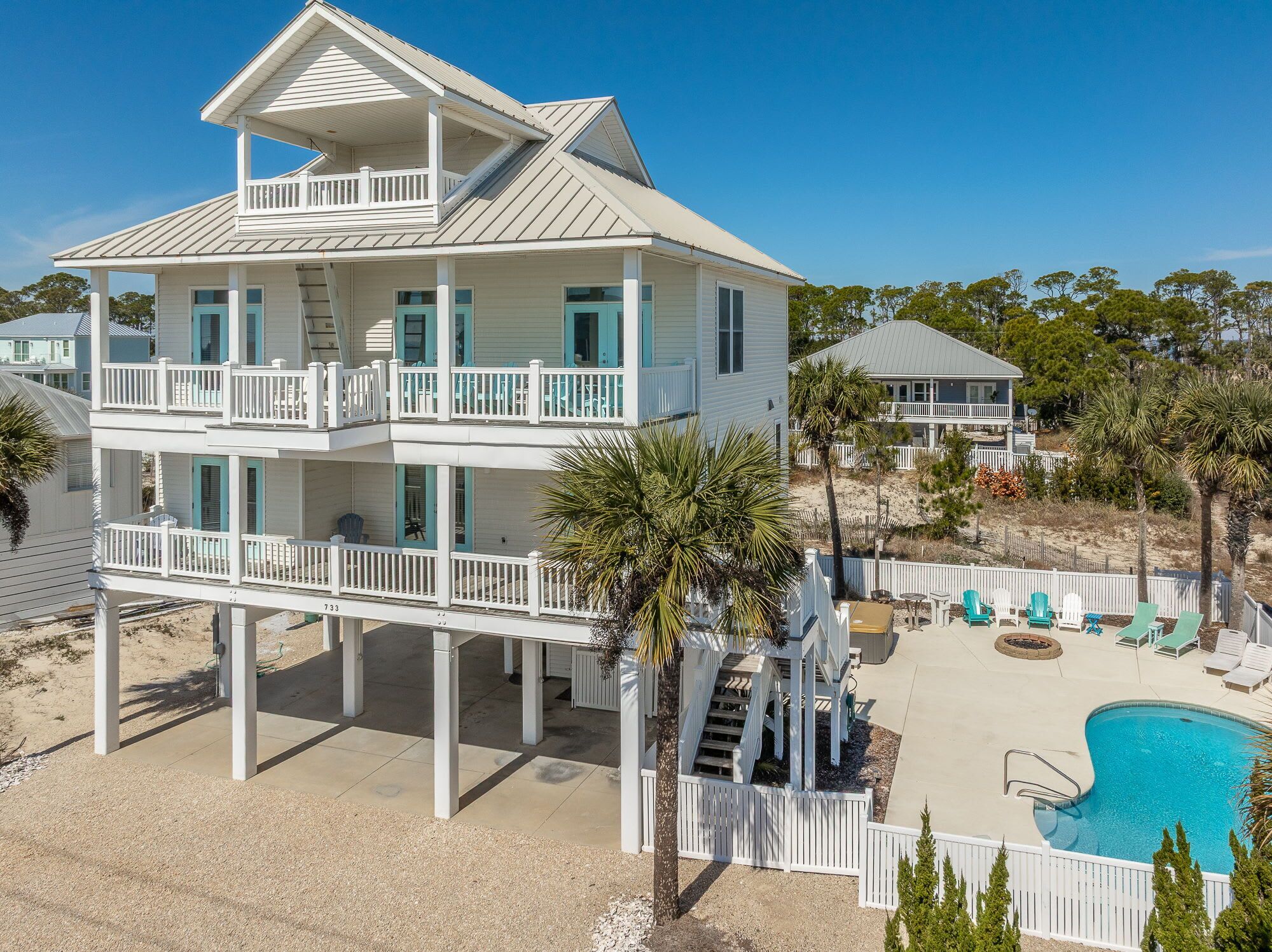 A two-story beachfront house with a balcony, a swimming pool, and a deck area.