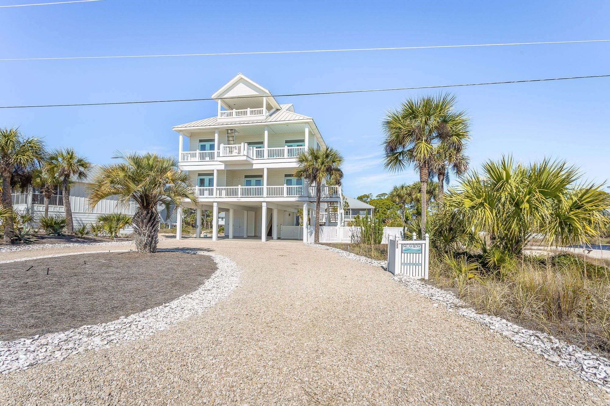 A multi-story beachfront property with a covered entrance and a gravel driveway leading to the main building.