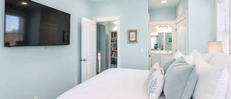 A bedroom with a bed, pillows, a ceiling fan, a TV, and a walk-in closet.