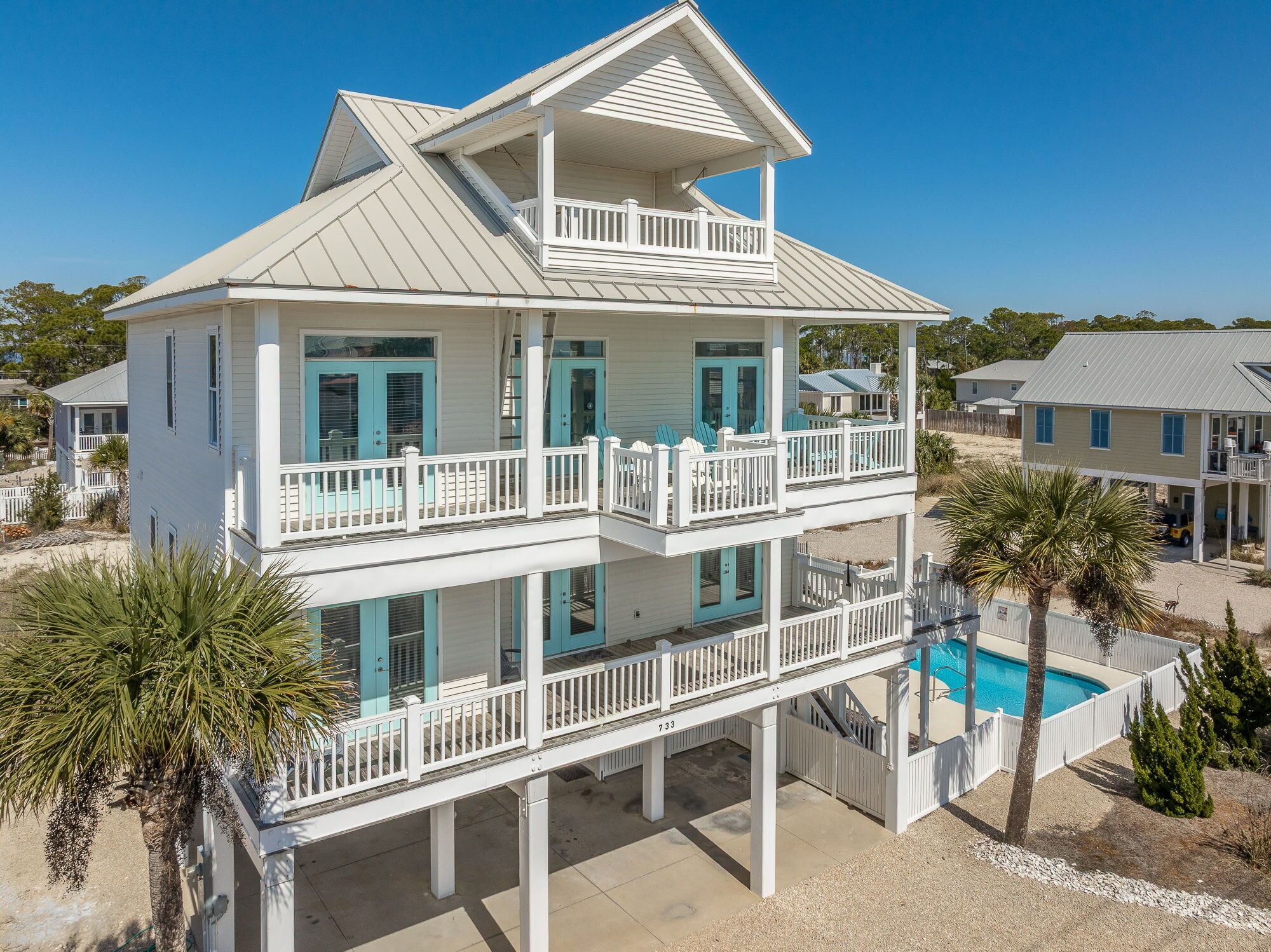 A two-story beachfront house with a balcony, a swimming pool, and a view of the ocean.