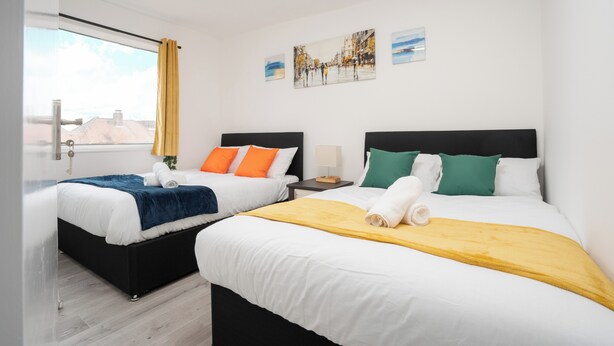 A hotel room with two beds, a window with curtains, and artwork on the wall. - 3 Bedroom House - Pool Table, Opp Train Station (Manchester)