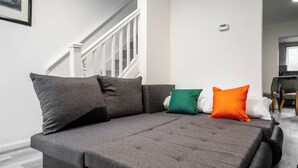 A grey sofa with multiple cushions in a room with a staircase and a chair. - 3 Bedroom House - Pool Table, Opp Train Station (Manchester)