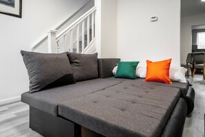 A grey sofa with multiple cushions in a room with a staircase and a chair. - 3 Bedroom House - Pool Table, Opp Train Station (Manchester)