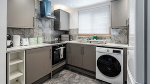 A compact kitchen with a built-in oven, a dishwasher, and a window with blinds. - 3 Bedroom House - Pool Table, Opp Train Station (Manchester)