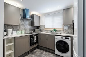 A compact kitchen with a built-in oven, a dishwasher, and a window with blinds. - 3 Bedroom House - Pool Table, Opp Train Station (Manchester)
