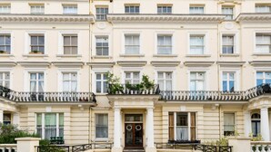 Ein mehrgeschossiges Gebäude mit einer symmetrischen Fassade, gleichmäßig angeordneten Fenstern und einem zentralen Eingang mit einer Tür und einem kleinen Balkon.