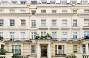 A multi-story building with a symmetrical facade, evenly spaced windows, and a central entrance with a door and a small balcony. - Notting Hill 3-Bed Apartment, Sleeps 6 with Wifi (London)