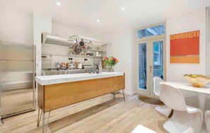 A modern kitchen with a central island, stainless steel appliances, and a dining area with white chairs. - Notting Hill 3-Bed Apartment, Sleeps 6 with Wifi (London)