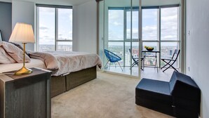 Ein modernes Schlafzimmer mit Bett, Nachttisch, Lampe und Blick auf die Stadt durch große Fenster.
