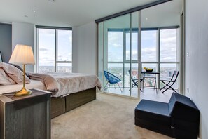 A modern bedroom with a bed, bedside table, lamp, and a view of the city through large windows. - Luxury City Apartment in Central London (London)