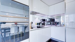 Eine moderne Küche mit weißen Schränken, einem Essbereich mit Glastisch und Stühlen sowie einem eingebauten Backofen.
