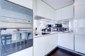 A modern kitchen with white cabinetry, a dining area with a glass table and chairs, and a built-in oven. - Luxury City Apartment in Central London (London)