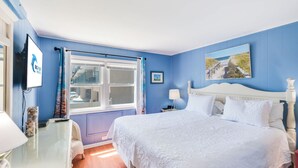 Quarto com cama grande, janela com cortinas, televisão na parede e quadro acima da cama.
