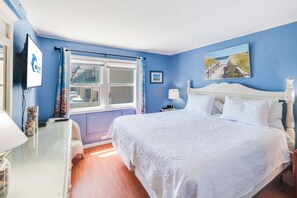 Ein Schlafzimmer mit einem großen Bett, einem Fenster mit Vorhängen, einem an der Wand befestigten Fernseher und einem Gemälde über dem Bett.