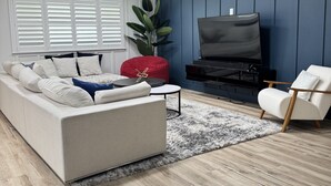 Una sala de estar moderna con un sofá modular, un otoman rojo, un televisor y un sillón blanco.