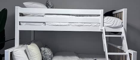 Una cama litera con escalera, ropa de cama blanca y un ventilador de techo.