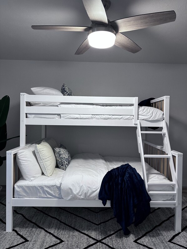 A bunk bed with a ladder, white bedding, and a ceiling fan.