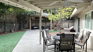 Un patio techado con mesa y sillas, un césped y una cerca de madera al fondo.