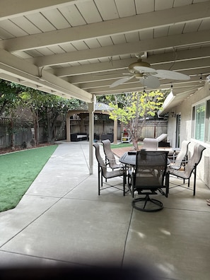 Un patio couvert avec une table et des chaises, une pelouse et une clôture en bois en arrière-plan.