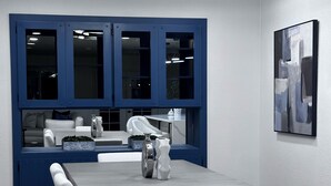 Un comedor con una mesa rectangular, sillas blancas, un armario azul con ventanas y una lámpara colgante moderna.