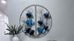 Una consola blanca con frentes de cajón geométricos, una obra de arte metálica en la pared, un florero con follaje verde y un cuenco de metal.