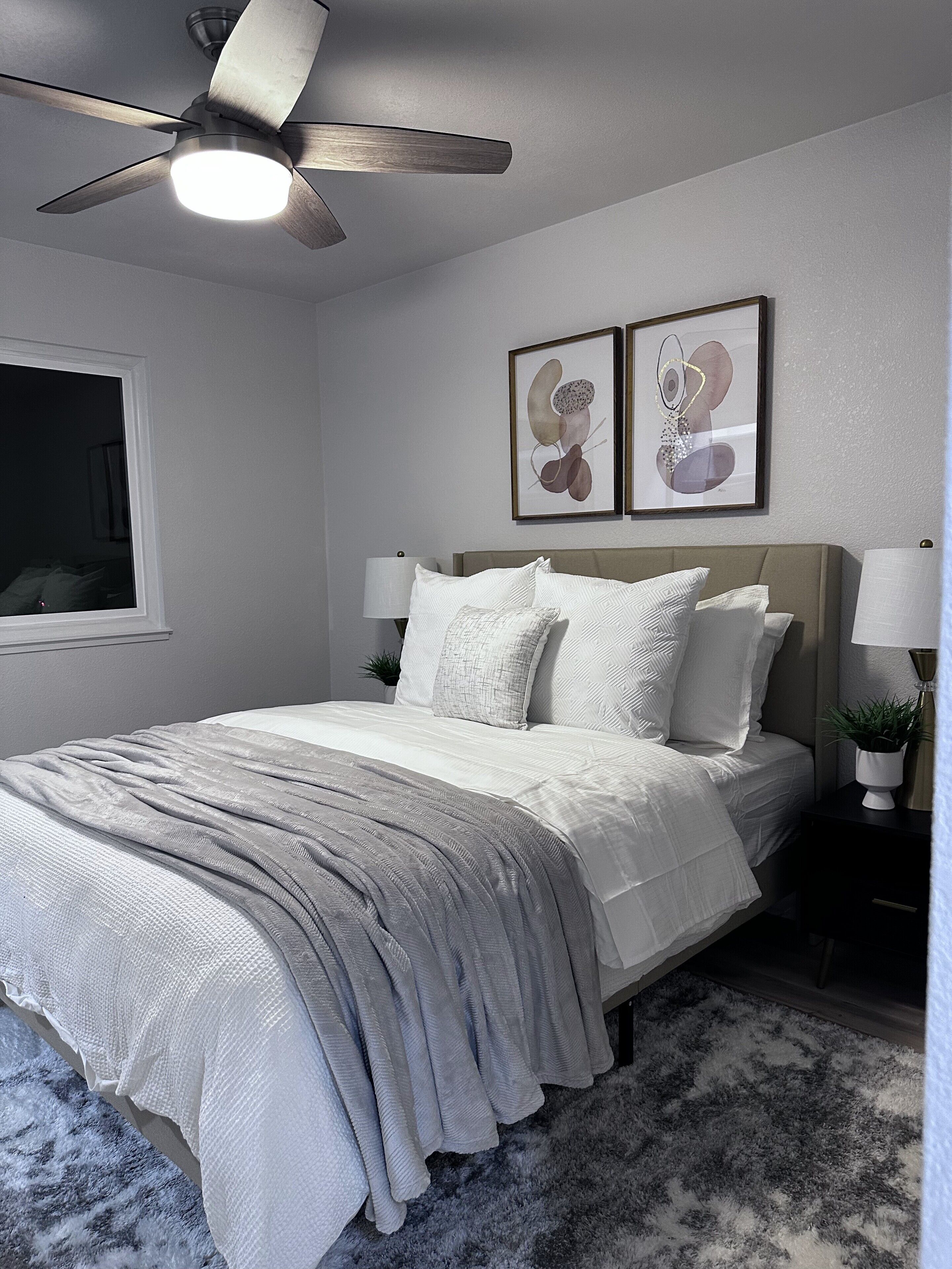 A bedroom with a bed, a ceiling fan, two wall-mounted lamps, and a window.