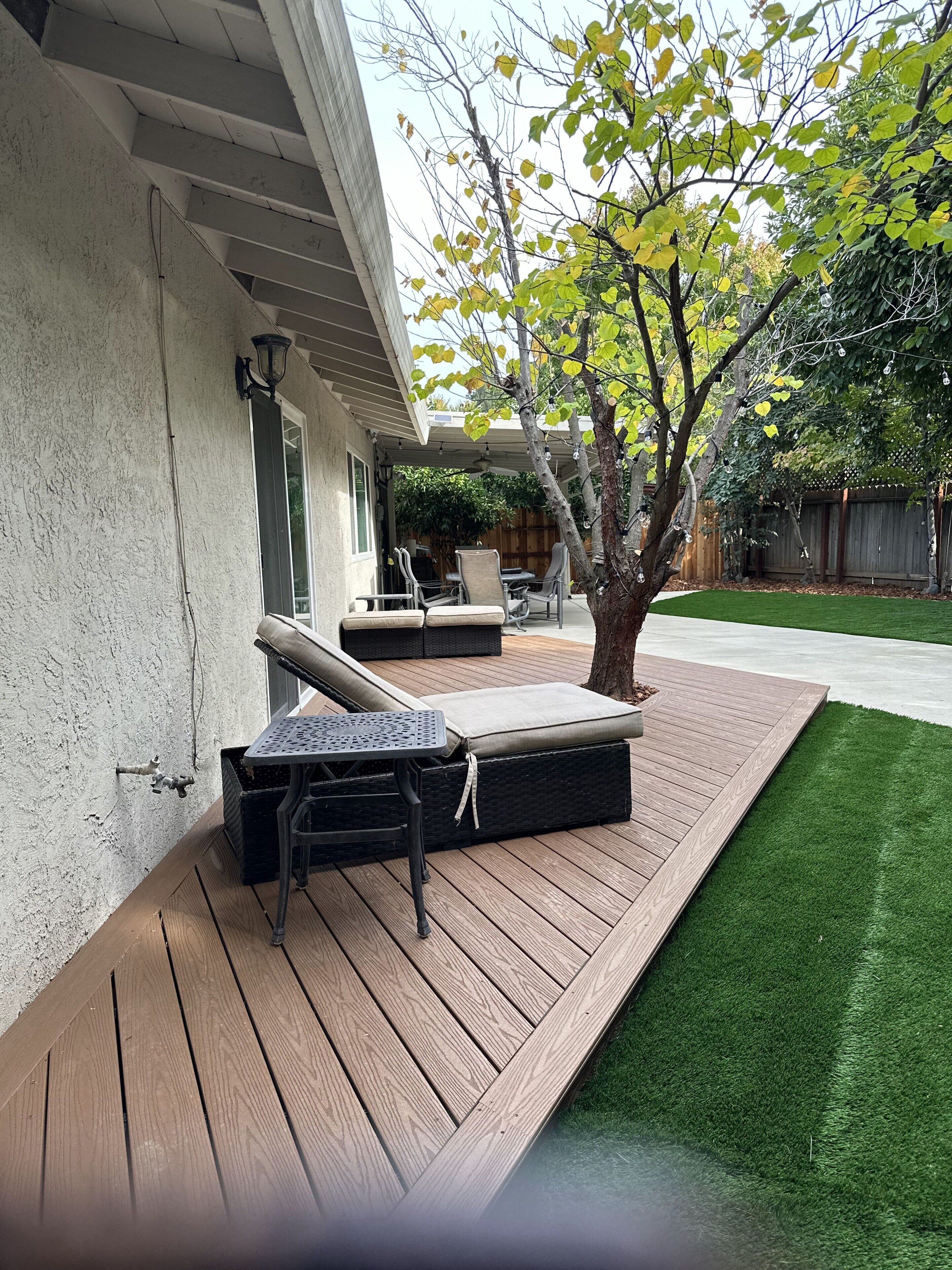 A covered patio with outdoor furniture, a tree, and a well-maintained lawn.