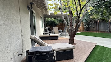 A covered patio with outdoor furniture, a tree, and a well-maintained lawn.
