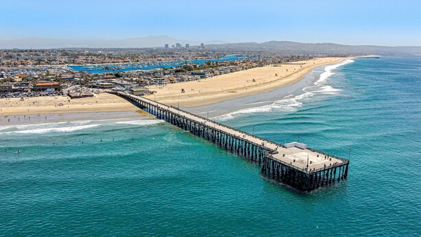 Un muelle que se adentra en el océano, con una playa y un paisaje urbano al fondo.