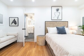 Ein Schlafzimmer mit Bett, Nachttisch, Lampe, einem gerahmten Bild an der Wand und einer Tür zum Badezimmer.