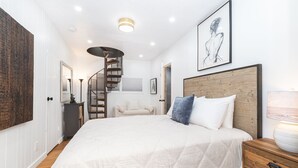 Un dormitorio con una cama grande, cabecera de madera, una escalera en espiral y una obra de arte enmarcada en la pared.