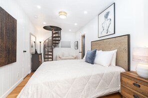 Ein Schlafzimmer mit einem großen Bett, einem Holzkopfstück, einer Wendeltreppe und einem gerahmten Kunstwerk an der Wand.