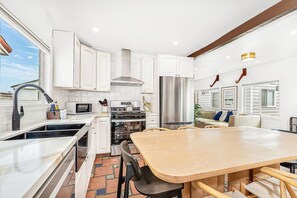 Une cuisine moderne avec des meubles blancs, un réfrigérateur en acier inoxydable et une table à manger en bois.