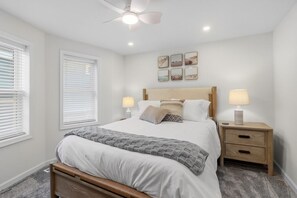 Een slaapkamer met een bed, bedlampen, een nachtkastje, een plafondventilator en decoratieve wandkunst.