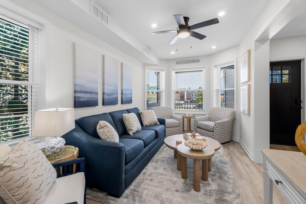 A modern living room with a blue sofa, a ceiling fan, and artwork on the walls.