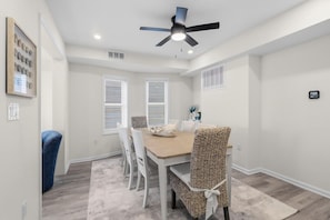 A dining area with a table, chairs, a ceiling fan, and a window with blinds. - North End 11BR - Walk to Beach & Boardwalk, Sleeps 26! (Ocean City)