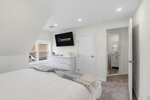 Une chambre à coucher comprenant un lit, une commode, un téléviseur fixé au mur et une porte donnant accès à une salle de bain.