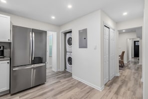 A modern kitchen with a stainless steel refrigerator, a washing machine, and a dining area with a chair. - North End 11BR - Walk to Beach & Boardwalk, Sleeps 26! (Ocean City)