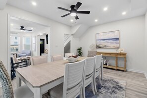 Un espace repas comprenant une table, des chaises, un ventilateur de plafond, un tableau et une console.