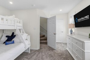 Ein Schlafzimmer mit Etagenbetten, einem Fernseher, einer Treppe und einer weißen Kommode.