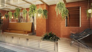 A modern outdoor seating area with a wooden bench and lounge chairs, surrounded by hanging plants and a ceiling with linear light fixtures. - BASE LAYER HOTEL KOBE SANNOMIYA (Kobe)