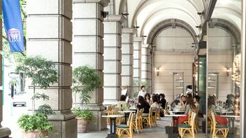 An outdoor cafe with stone columns, potted plants, and tables with chairs.
